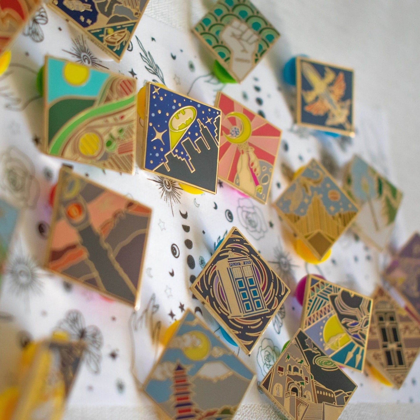 There are several diamond shaped pins made of gold metal, each with a design on which represents locations in fiction.