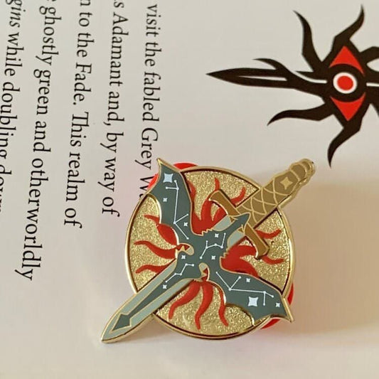 A round pin with recessed metal has a sword ontop of it facing vertically. Ontop of the sword is a grey dragon which features a white constellation print ontop of it. Behind the sword is the chantry symbol printed in red.