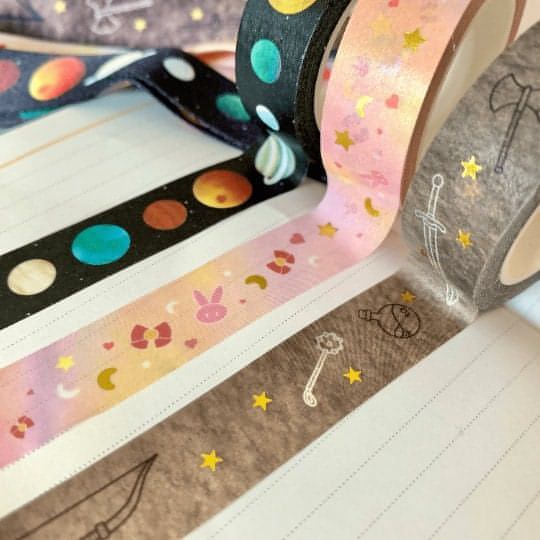 Three washi tape designs are rolled onto a piece of paper side by side. From left to right: galactic, anime, and fantasy.