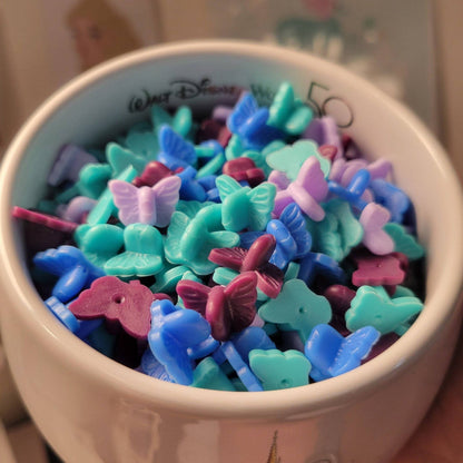 In this photo there are dozens of different colour butterfly shaped rubber pink backs. They're in blue, pink, and purple. They are in a cup or bowl.