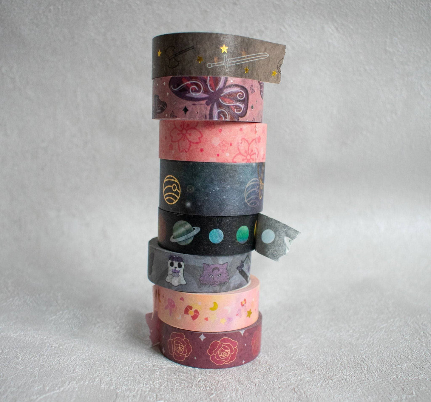 This photo is a clearer image of the stacked washi tape. They are all the tapes I've made as of January 2022. They are in order from top to bottom: fantasy, butterflies, sakura, celestial, galactic, spooky, anime, and roses.