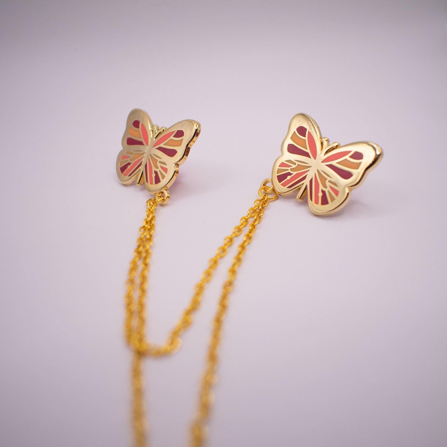 The image is a medium-distance photo of the pink and orange butterfly collar pin. Both pins are pictured and the chain length is shown also (the chains are 10cm and 15cm respectively).