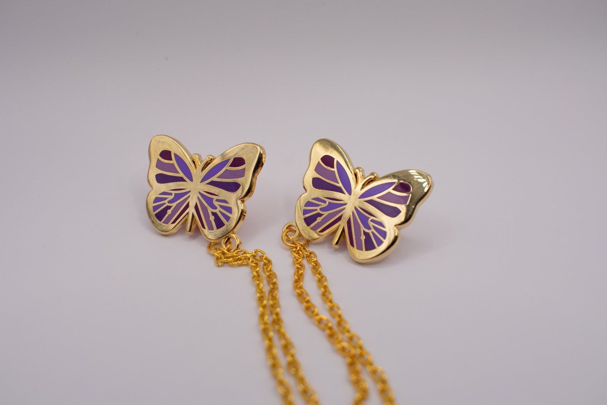 This is a medium distance shot of the purple butterfly collar pin. Both butterflies are pictured with the chain length visible. 